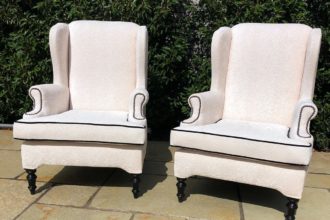 A pair of old winged arm chairs recovered in a Linwood fabric - with contrast black piping detail