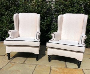 A pair of old winged arm chairs recovered in a Linwood fabric - with contrast black piping detail